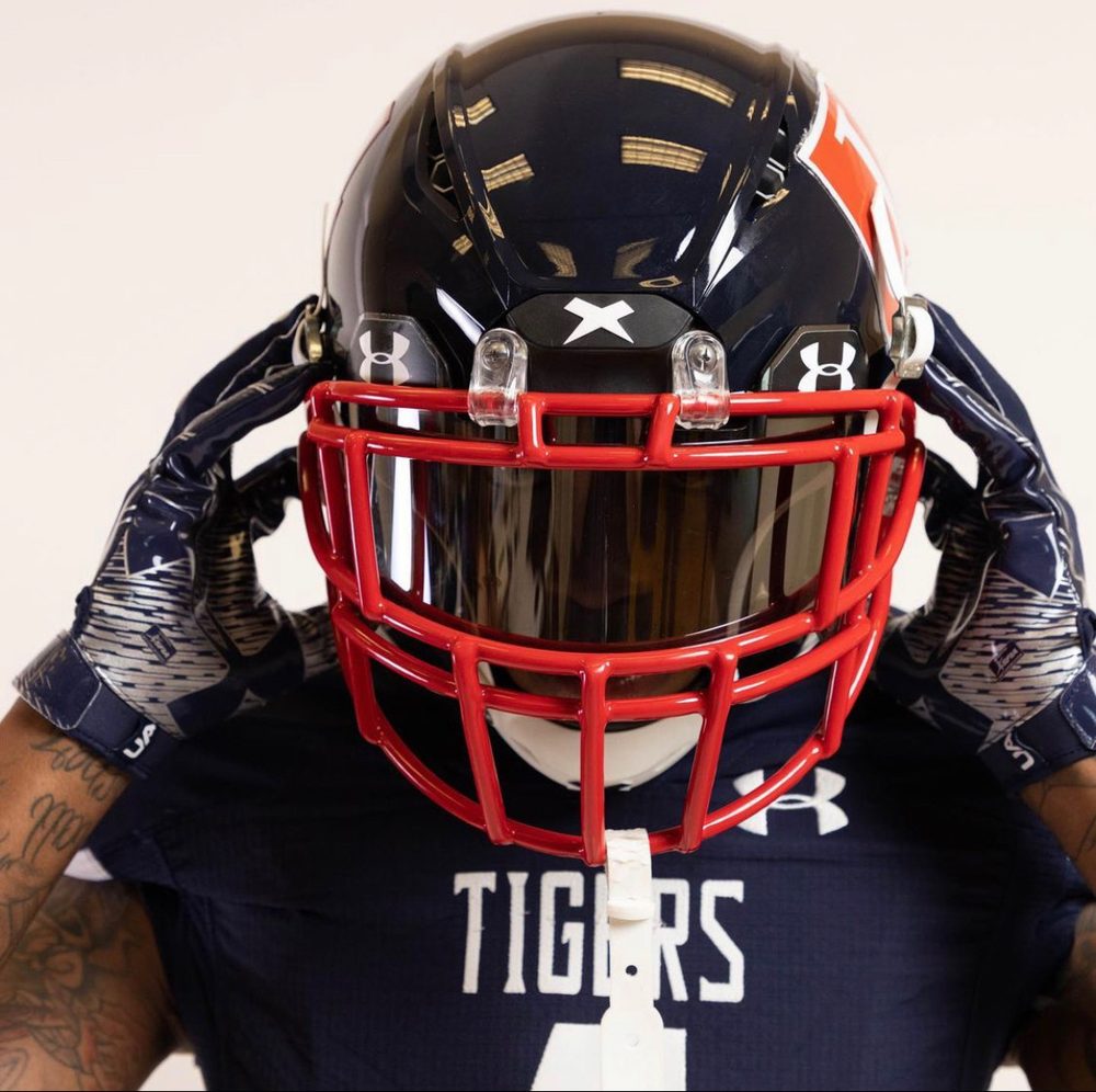Football player adjusting a navy helmet with a red facemask
